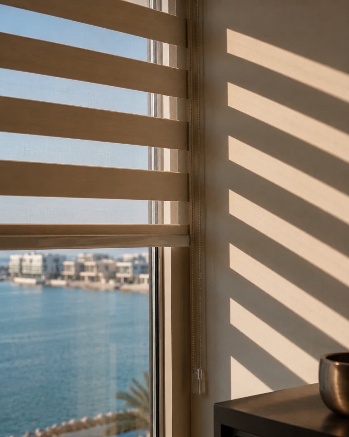 Zebra blinds half-drawn over a waterfront window, striped light on the wall