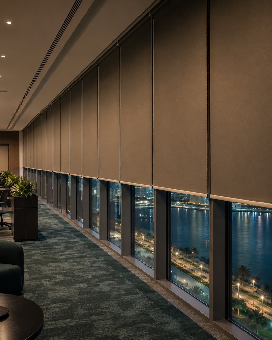 Office floor at dusk with roller blinds lowered across a wall of windows